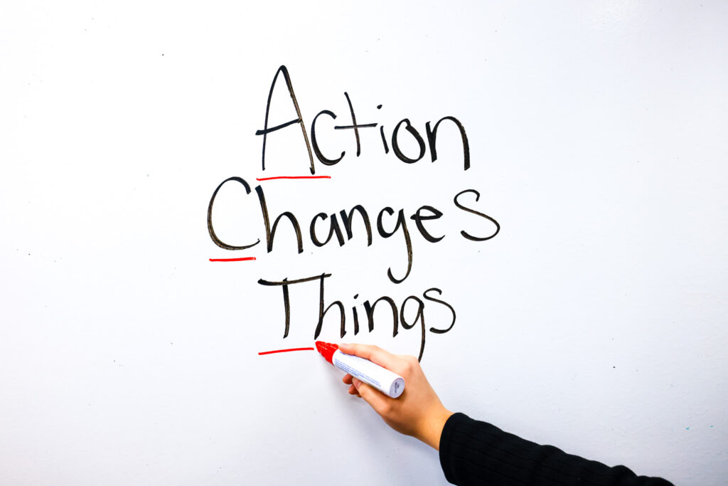 A hand writes the words action changes things, with the first letter of each word underlined in red to spell the word act.