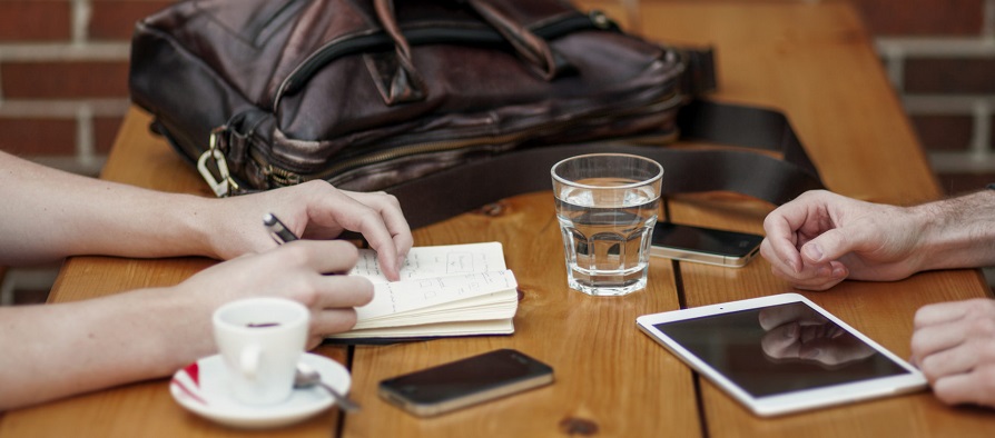 Two people at table with computer bag, mobile devices, and cups brainstorming how to drive social media engagement.