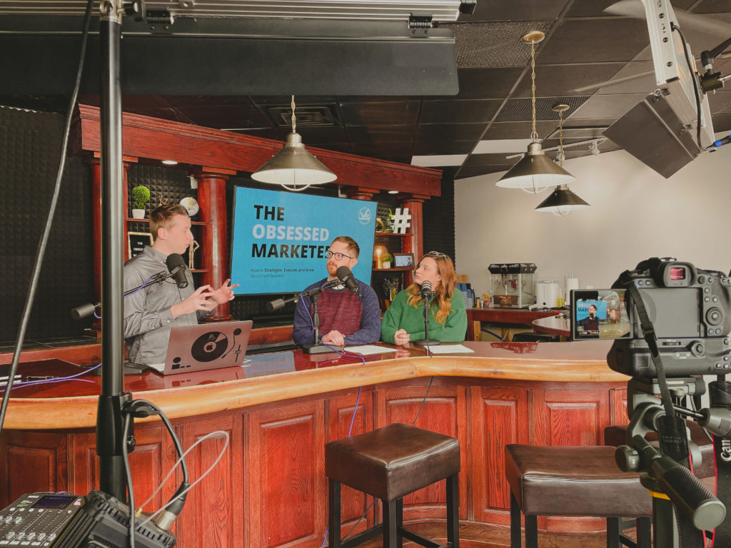 Viral Solutions marketing team records an episode for The Obsessed Marketer podcast with video equipment.
