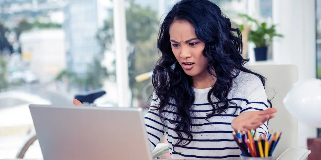 frowning dark-haired woman looking at laptop with hands slightly raised