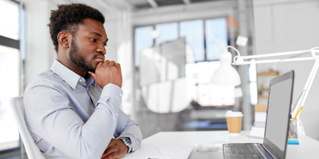 Businessman in office looking at laptop and contemplating how to handle social media bullying. 