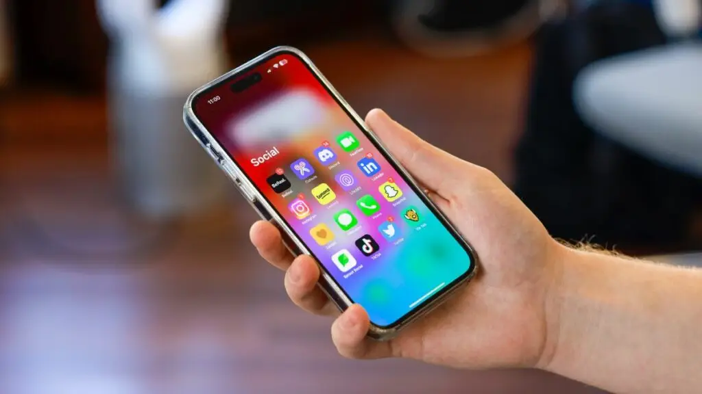 Hand holding a smartphone displaying social media icons.