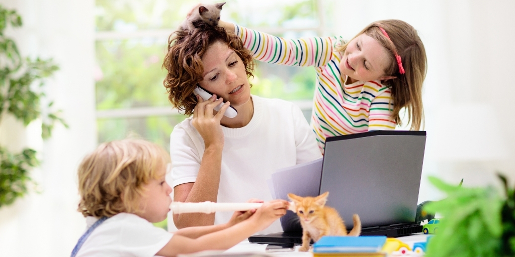 Mother on phone in front of laptop while children pull her hair and play music.