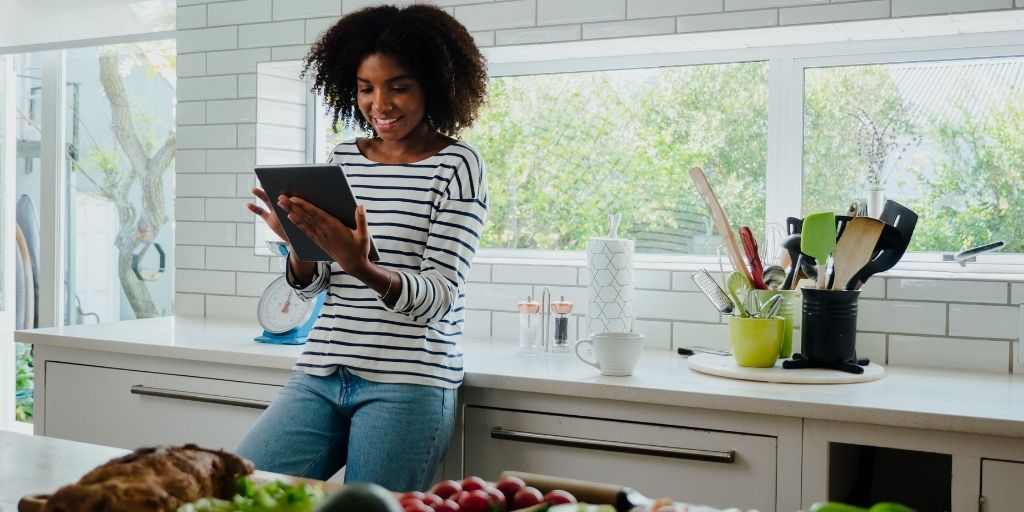 Woman researching recipes on digital tablet while leaning against the counter in her kitchen.