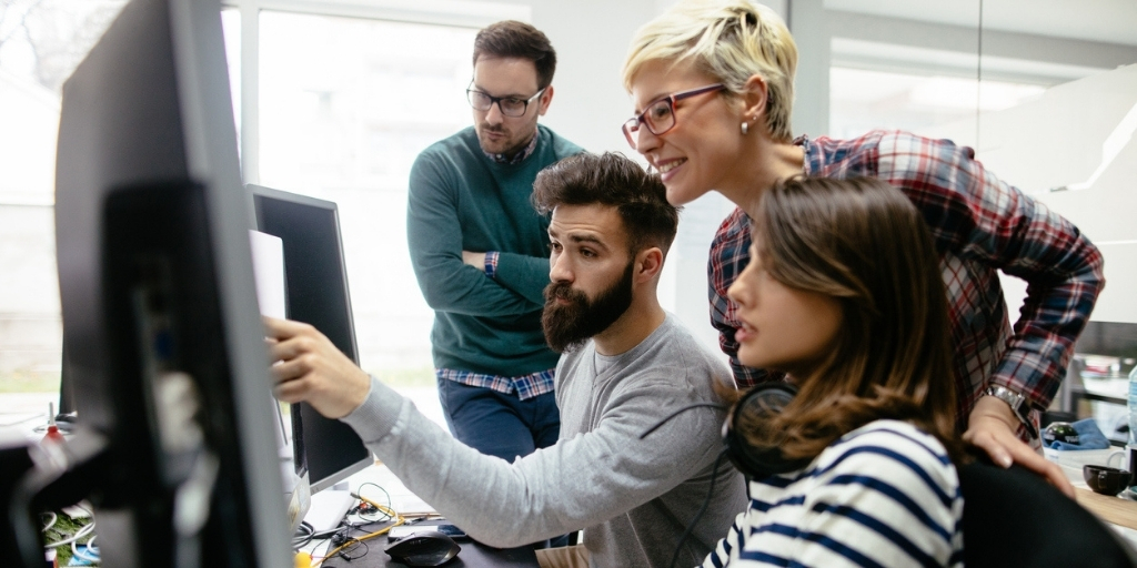 Group of coworkers gathered around computer working on web page design.