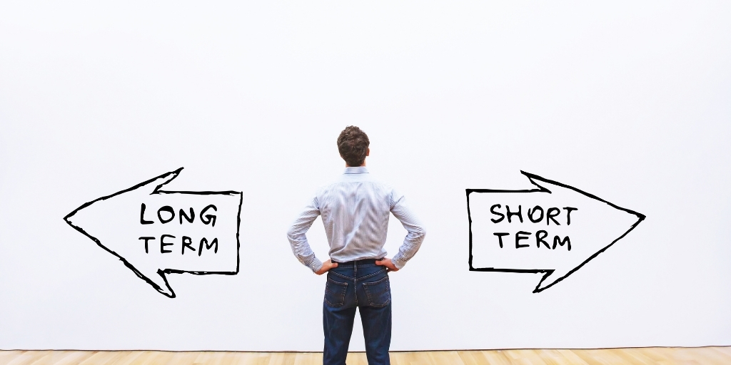 Man standing in front of wall with two arrows labeled long term and short term pointing in opposite directions.