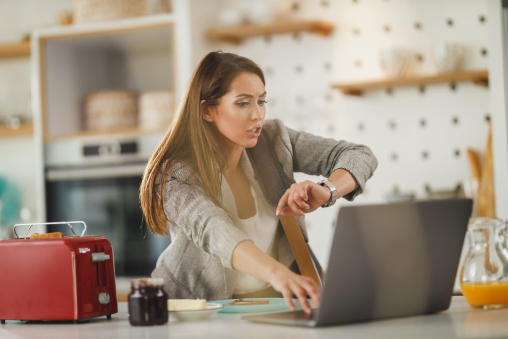 Businesswoman looks at her watch while urgently checking her schedule on a laptop computer.