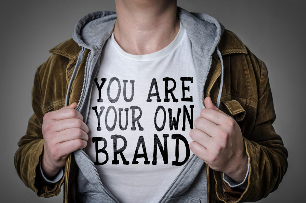 Man with coat open showing t-shirt that says you are your own brand as concept of personal brand vs. company brand.