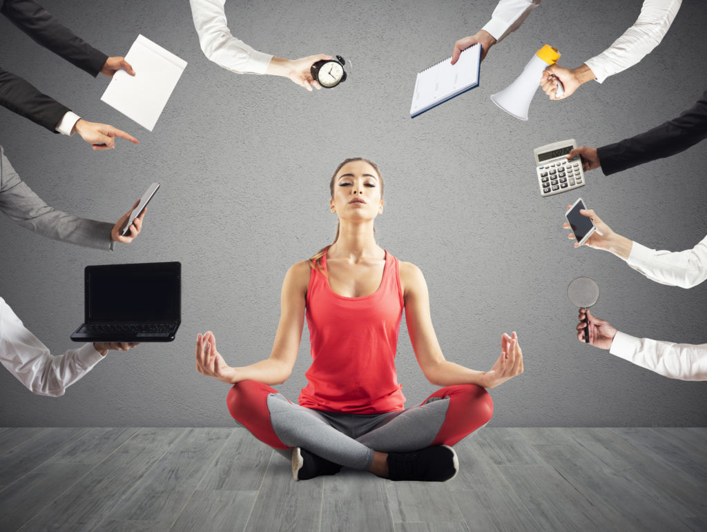 Woman doing yoga surrounded by arms holding various devices to demand her attention.