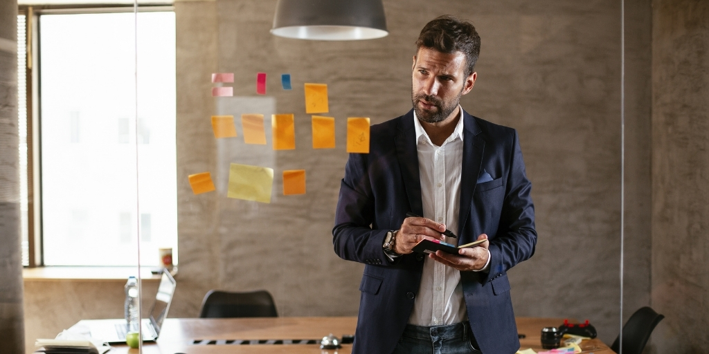 Male business professional standing in front of glass with sticky notes, outlining process for adapting to market changes.