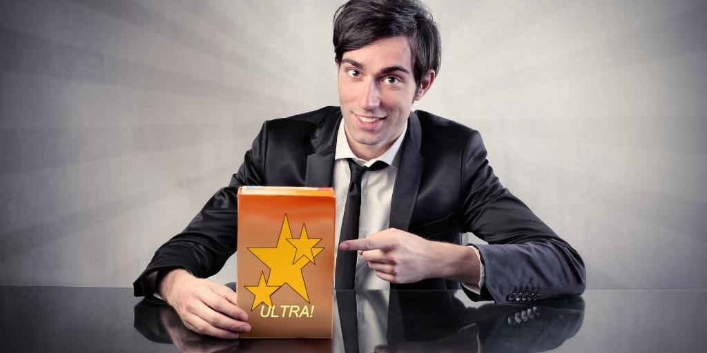 A man in a suit with a loosened tie points to a box with stars with the word Ultra on it.