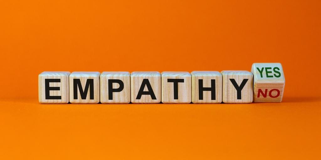 The word empathy spelled out in wooden blocks with a final block teetering between the words yes and no.