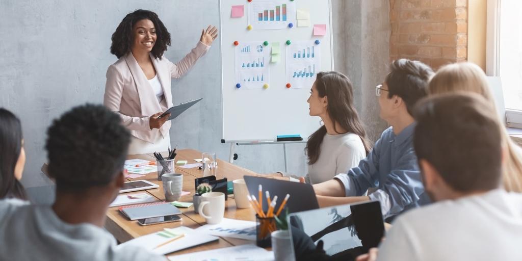 Female marketer gesturing to whiteboard with graphs during business presentation.