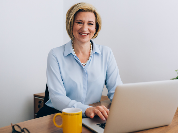 Middle-aged female insurance agent smiling and using laptop in her office.
