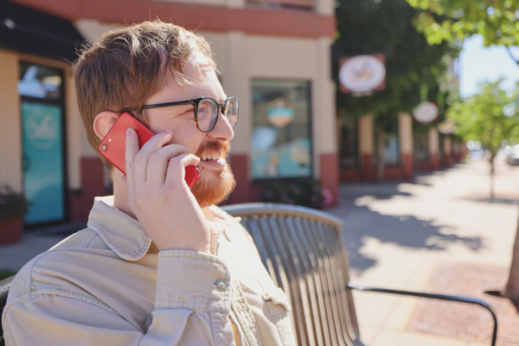 Joel from Viral Solutions smiling while talking on phone outside on a bench.