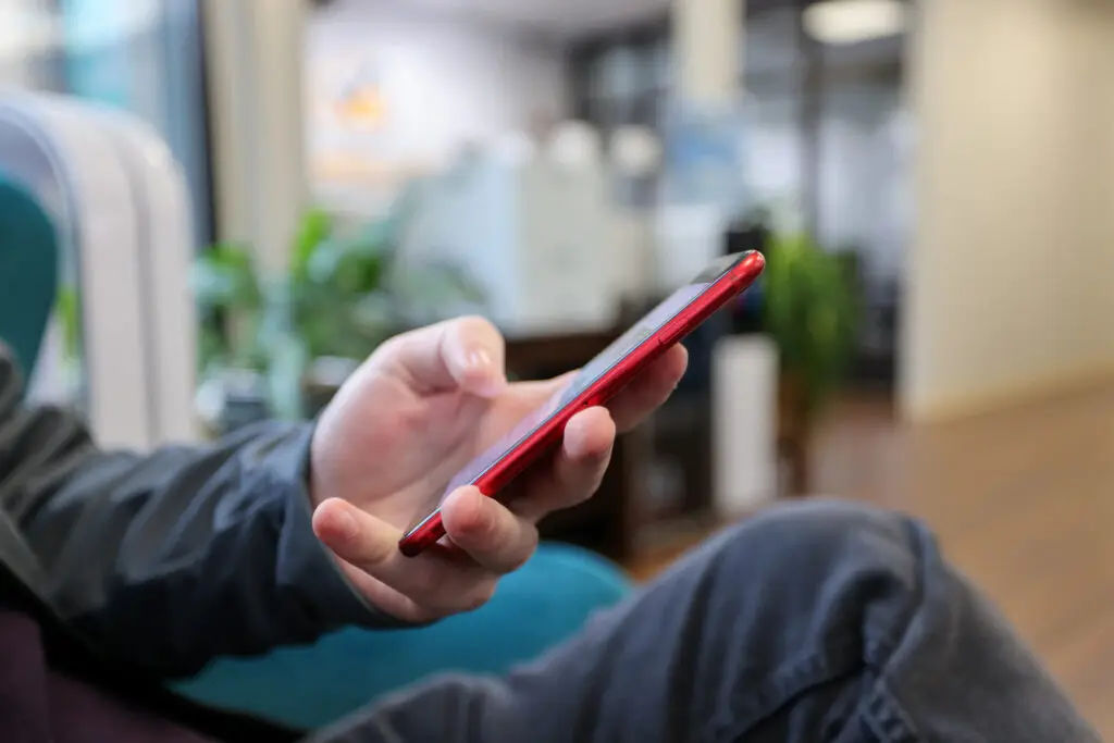 Close-up of hand holding red smartphone as individual browses social media.