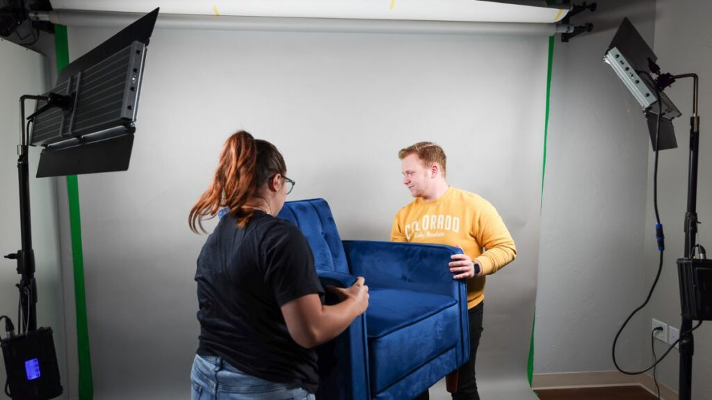 Holland and Andrew of Viral Solutions moving a blue couch in front of a white background for video filming.