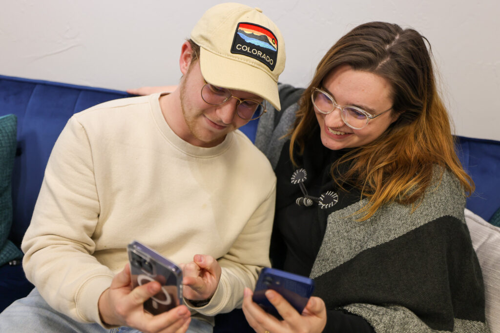 Two people enjoy watching videos on their smartphones on a couch.