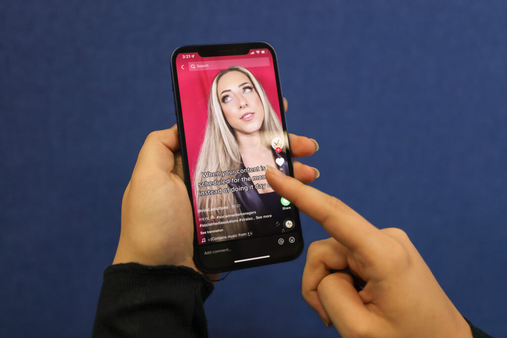 A fan holds a phone vertically and points to the screen showing a social media influencer video.