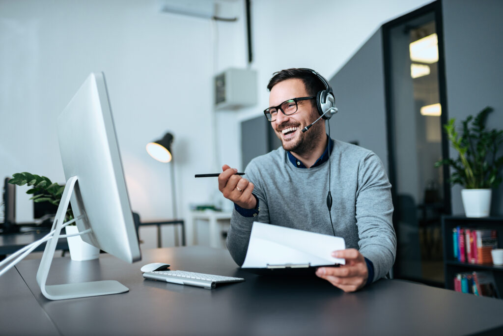 Smiling man in glasses wearing a headset and conducting referral prospecting over the phone.