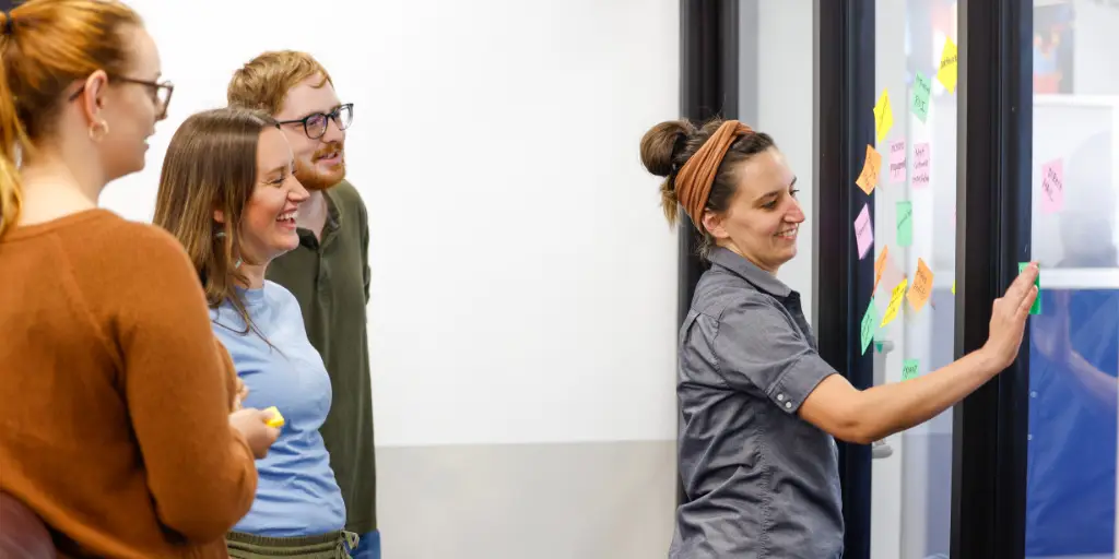 Joel, Meagan, and Taylor of Viral Solutions watching as Lindsey communicates strategy with sticky notes in the conference room.