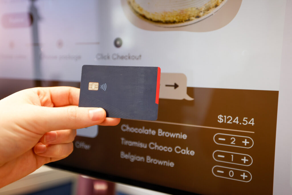 A man holds up a credit card to check out a food order using a self-serve kiosk.