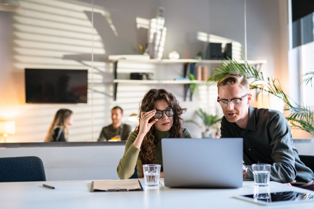 A male and female professional look at a laptop while discussing their sales enablement strategy.