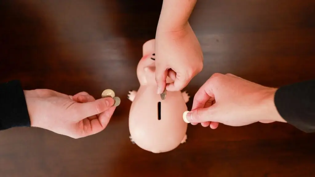 Three hands putting coins into a piggy bank. 